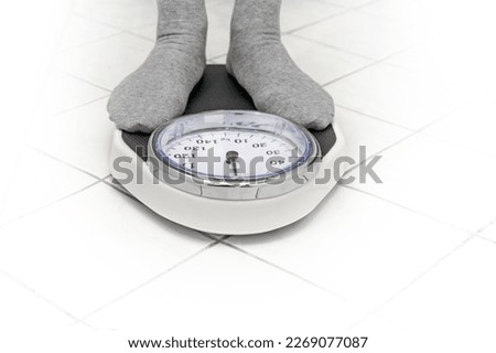 Feet in gray socks standing on a personal scale on the white tiled bathroom floor for weight measuring, copy space, selected focus