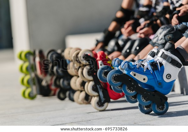 Feet of\
group childrens wearing inline roller skates sitting in outdoor\
skate park, Close up view of wheels befor\
skating