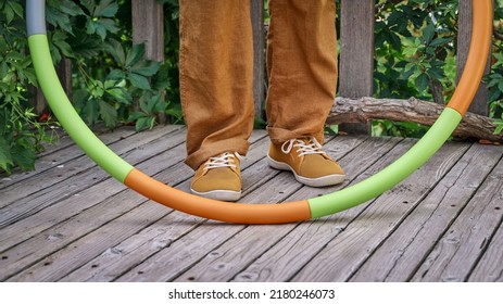 Feet And Leg Of A Man With Weighted Hula Hoop On A Wooden Backyard Deck In Summer Scenery, Core Workout Concept