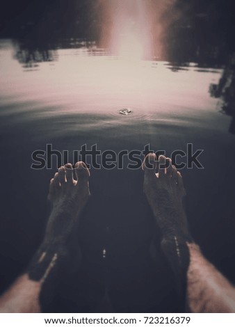 feet and legs relaxing in water at sunset on a summer day with reflection 