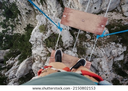 feet of a male tourist crossing a abyss in the mountains on a suspension bridge