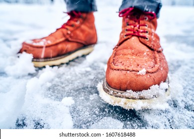 Feet of a man on a snowy sidewalk in brown boots. Winter slippery pawement. Seasonal weather concept