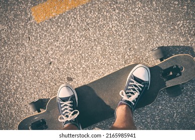 Feet of man in sneakers on a double kick cutaway longboard in the city in the evening