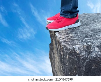 The feet of a man wearing sneakers standing on a cliff