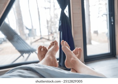 The feet of a married couple sticking out from under the blanket in a country house with panoramic windows. - Powered by Shutterstock