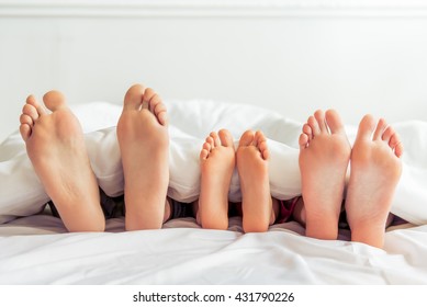 Feet of mother, father and their little daughter lying on bed covered with blanket