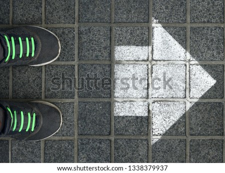 Feet on the cobblestone. gray sporty sneakers on the road with painting white arrow. way of runner