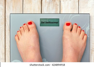 Feet on scale with text You are beautiful in Italian language on the wooden background. Foot with nail polish.Beauty and weight.Obesity in Italy on scale.
