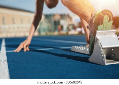 Feet On Starting Block Ready For A Spring Start.  Focus On Leg Of A Athlete About To Start A Race In Stadium With Sun Flare.