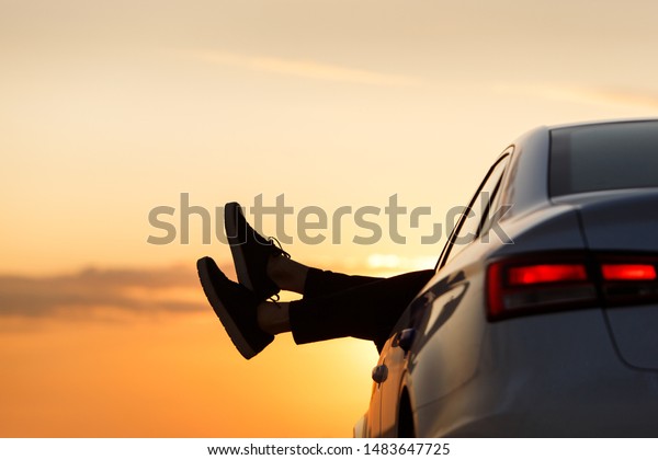 Feet\
outside the window at sunset, copy space. Man driver put feet on\
car door, relaxing, resting, enjoying the moment, feeling the air\
and freedom. After covid-19, back to normal life.\
