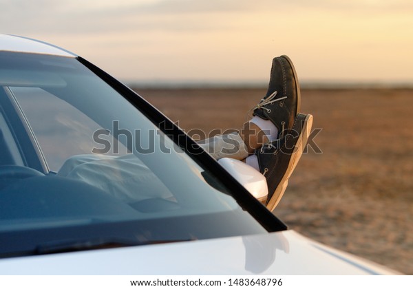 Feet outside the window at sunset, copy\
space. Man driver put feet on car door, relaxing, resting, enjoying\
the moment, feeling the air and freedom.\
