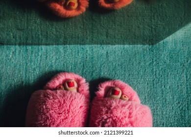 Feet With Painted Red Toenails In Pink Fuzzy Slippers On Teal Carpet