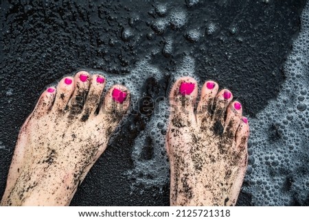 feet with pink painted toenails dirty with wet black sand in bubbly water at the beach