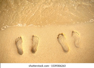 Feet Prints On The Sand Of The Beach And Sea Wave. Top View. Two People Foot Marks On Sand. 