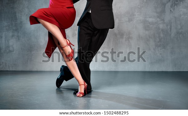 Feet of professional tango dancers in\
dancing movement on bright background\
indoors