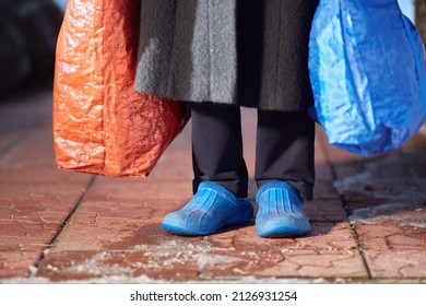feet of refugees or homeless people in dirty cheap shoes. A faceless woman with large bags in her hands