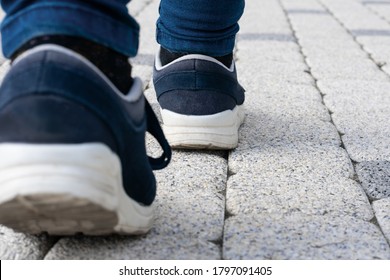 Feet In Running Shoes Are Walking Forward On Stony Road. Concept Of Leaving, Loneliness Or Passing Away