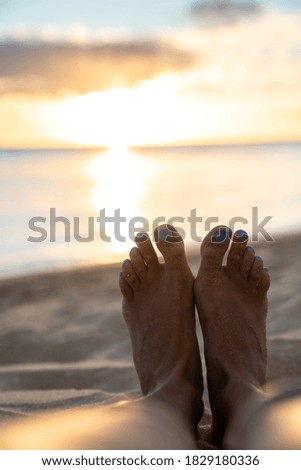 Feet in the sand and sunset over the ocean