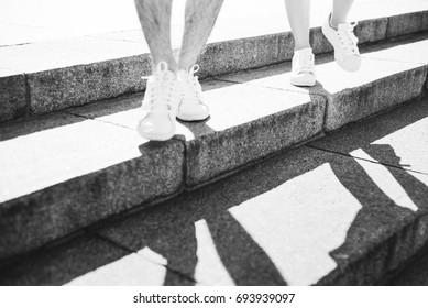 Feet And Shade Of Two People Walking On Stairs In Sport Shoes Black And White