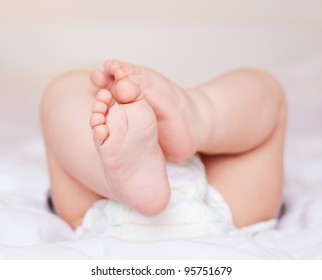 Feet Of A Six Months Old Baby Wearing Diapers Lying In Bed At Home