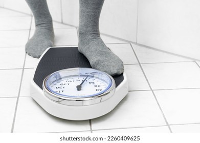 Feet in socks stepping on a personal scale on the tiled bathroom floor to measure the body weight, copy space, selected focus