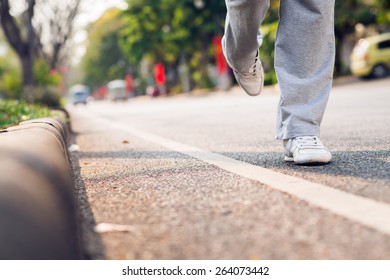 Feet of sportswoman running along the road