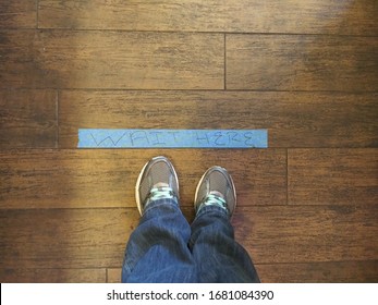 Feet Standing By A Message That Reads Wait Here