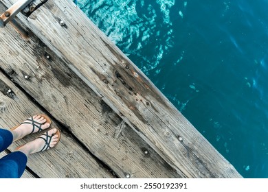 Feet standing on a wooden pier above clear blue water at a serene lake during a sunny day - Powered by Shutterstock