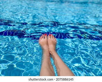 Feet In Swimming Pool Water. Selfie Of Legs And Barefoot With Red Pedicure And Manicure Nails On Blue Sea Background. Vacation At Summer Holiday.