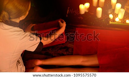 Feet Thai massage. Cropped shot of foot reflexology. Body part of female hand and leg on candels background. Masseuse in foreground in spa salon room.