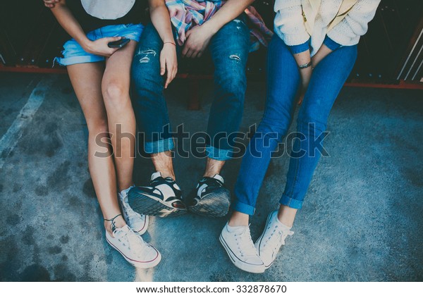 Feet of three friends sitting together. Cropped\
portrait of two girl and one boy relaxing. Top view of shoes of\
hipsters resting.