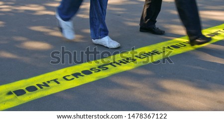 Feet of two women crossing a line with warning written on the ground