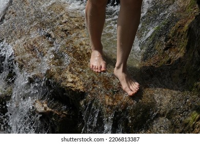 Feet In The Water Closeup.A Person Walking Barefoot On The Wet Stones Of A Waterfall