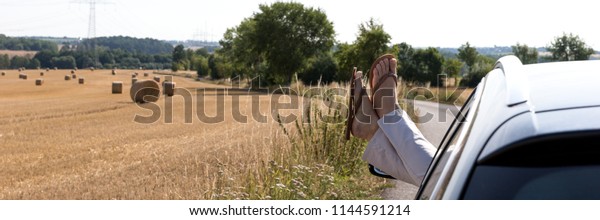 Feet of woman with flip flops through the open window\
of the car