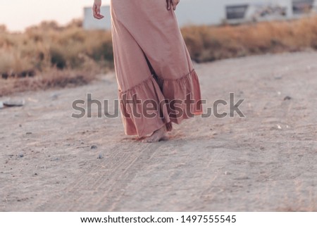 feet of a woman in a pink dress walking on the sand during sunset