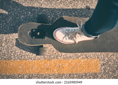 Feet of woman in sneakers on a double kick cutaway longboard in the city in the evening