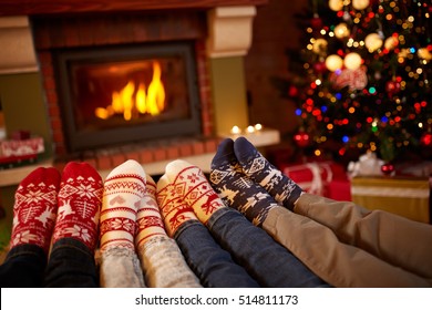 Feet in wool socks near fireplace in winter, family at home near fire