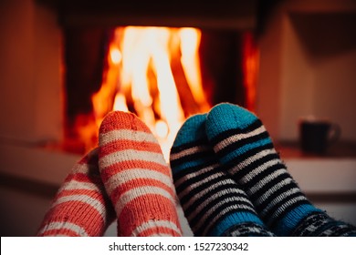Feet in wool striped socks by the fireplace. Relaxing at Christmas fireplace on winter holiday evening.