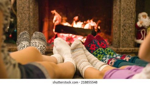 Feet In Woolen Socks Warming By Cozy Fire In Christmas Time. Family With Two Kids Warming Their Feet By The Fireplace In Winter Time. 