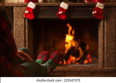 Feet In Woollen Socks By The Christmas Fireplace. Woman Relaxes By Warm Fire And Warming Up Her Feet In Woollen Socks. Close Up On Feet. Winter And Christmas Holidays Concept. 