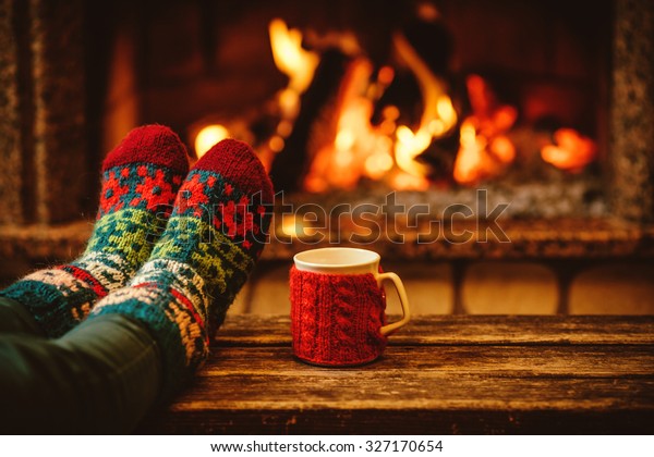 Feet in woollen socks by the Christmas\
fireplace. Woman relaxes by warm fire with a cup of hot drink and\
warming up her feet in woollen socks. Close up on feet. Winter and\
Christmas holidays\
concept.
