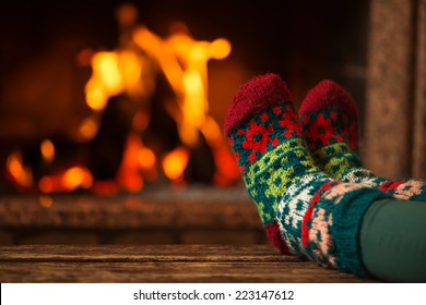 Feet in woollen socks by the fireplace. Woman relaxes by warm fire and warming up her feet in woollen socks. Close up on feet. Winter and Christmas holidays concept. 