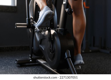 Feet of young female athlete exercising on elliptical trainer machine in the gym. Athletic woman cycling indoors on modern orbitrek equipment - Powered by Shutterstock