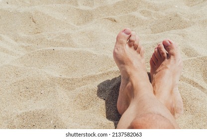 Feet Of Young Man Sunbathing On The Beach Sand.