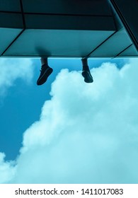 Feet Of Young Man Who Sits On Ledge Of Skyscraper, Facing Clouds And Blue Sky, For Urban, Travel, Or Psychological Concepts (selective Focus)