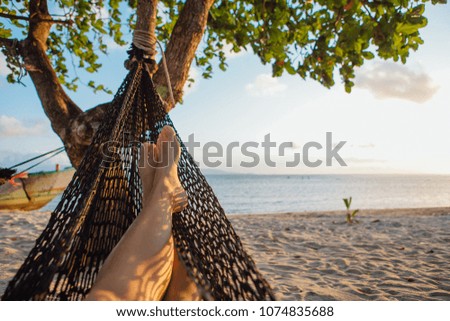 Feet of a young woman in hammock on the beach under the tree