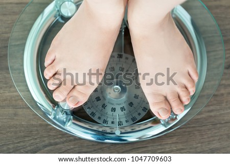 Feet of a young woman measuring her weight on a bathroom scale