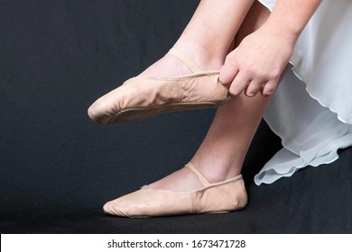 feet of a young woman putting on ballet slippers.