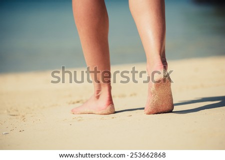 The feet of a young woman as she is walking on the beach