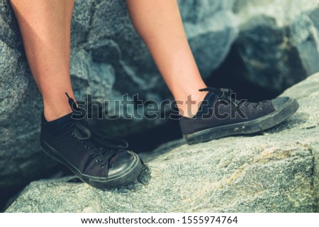 The feet of a young woman wearing black shoes sitting on a rock